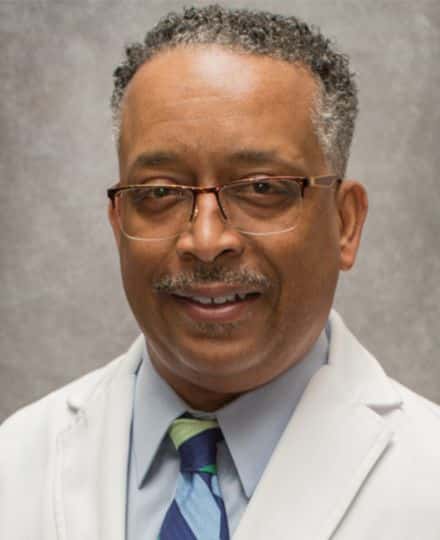 Headshot of dr. Hector cooper wearing a white medical coat and glasses.