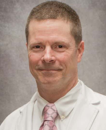 Headshot of dr. Michael smith wearing a white medical coat and pink patterned tie.