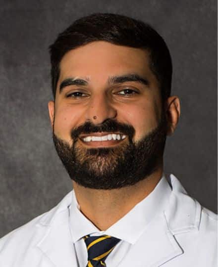 Headshot of dr. Mobeen reza wearing a white medical coat and striped tie.