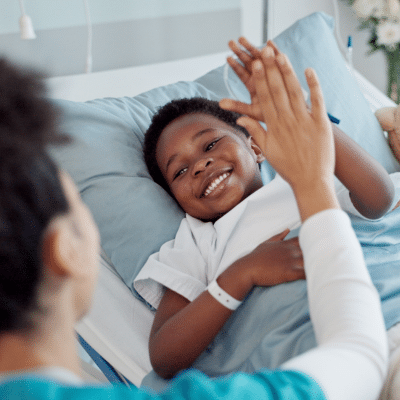 Little boy lying in a hospital bed giving high five to a woman, representing non-invasive pediatric imaging
