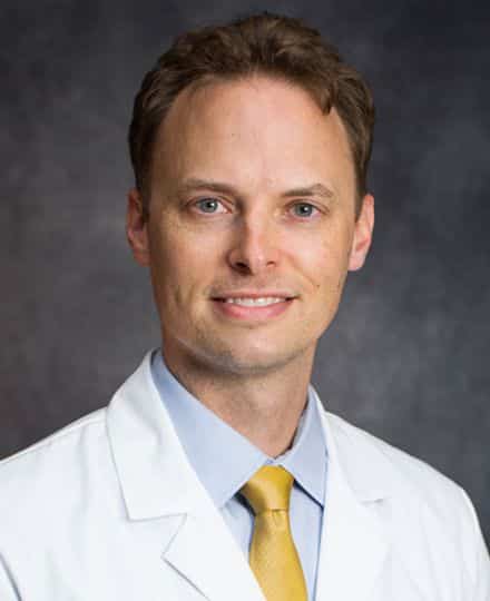 Headshot of dr. Adam lustig wearing a white coat and yellow tie.