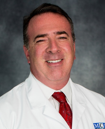 Adam specht, md smiling against a grey background.