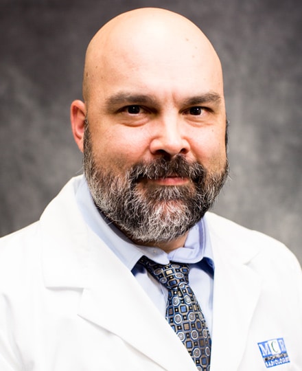 Andrew gray, pa-c. Professional headshot of a medical provider in a white coat and patterned tie, standing against a gray studio background.