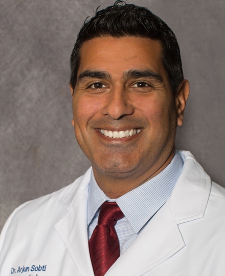Arjun sobti, md smiling in front of a professional grey backdrop.