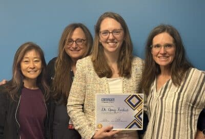 Group photo of dr. Amy farkas holding her chkd excel award certificate, standing with three colleagues against a blue wall.