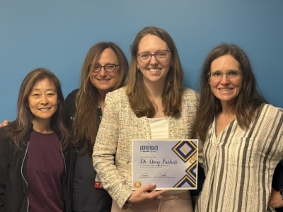 Group photo of dr. Amy farkas holding her chkd excel award certificate, standing with three colleagues against a blue wall.