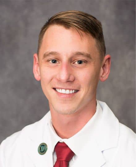 Professional headshot of a medical provider wearing a white coat against a neutral gray background.
