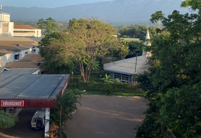 View of a hospital campus in tanzania with trees, emergency entrance, and mountains in the distance, photographed during dr. Amy farkas’ rad-aid global radiology volunteer trip.