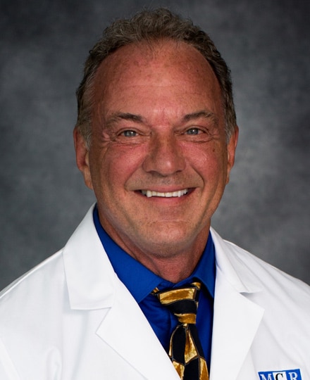 Daryl fanney, ph. Professional headshot of a male radiologist with thinning hair wearing a white medical coat and smiling against a neutral gray background.