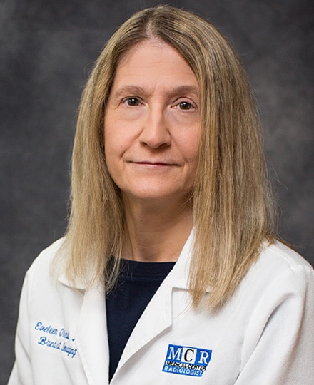 Eveleen oleinik, md smiling in her white coat in front of a backdrop.