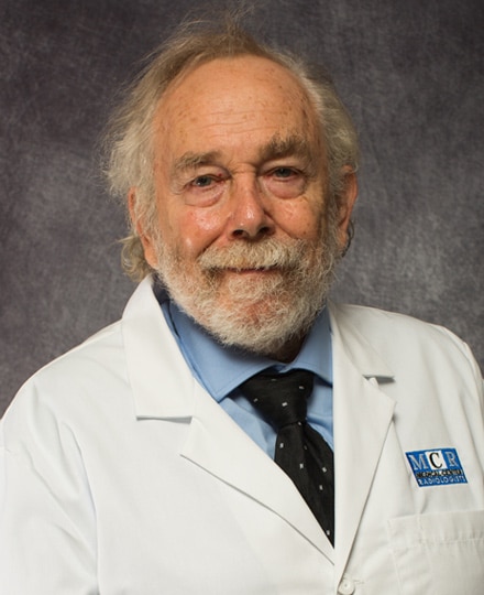 Jeffrey crass, md. Professional headshot of an older male radiologist wearing a white medical coat, light blue shirt, and dark tie, posed against a neutral studio background.