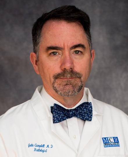 John campbell, md. Professional headshot of a male radiologist wearing a white medical coat and patterned bow tie, standing in front of a neutral studio background.