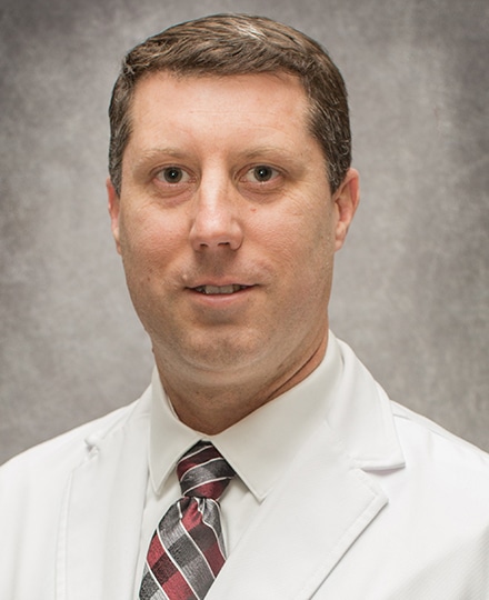 Meet dr. Justin day, do. Professional headshot of a male radiologist wearing a white medical coat and patterned tie, posed against a neutral gray background.