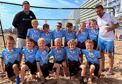 Young boys’ beach soccer team wearing mcr-branded jerseys posing with their coaches in virginia beach.