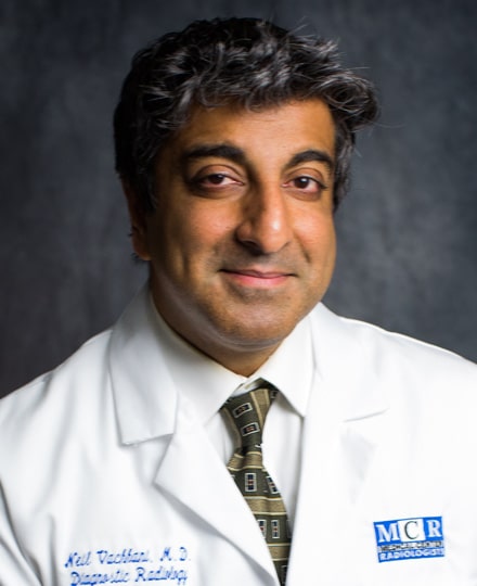 Neil vachhani, md smiling against a professional grey background.