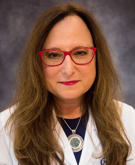 Rachel pevsner crum smiling in her white coat in front of a gray backdrop.