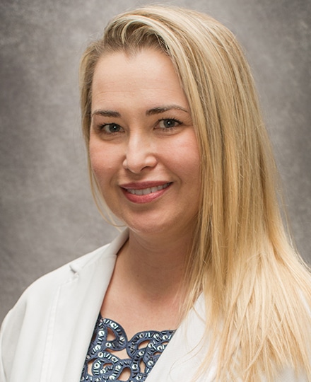 Sarah bumps, md, mba, ph. Professional headshot of a female radiologist wearing a white medical coat, smiling in front of a neutral studio background.