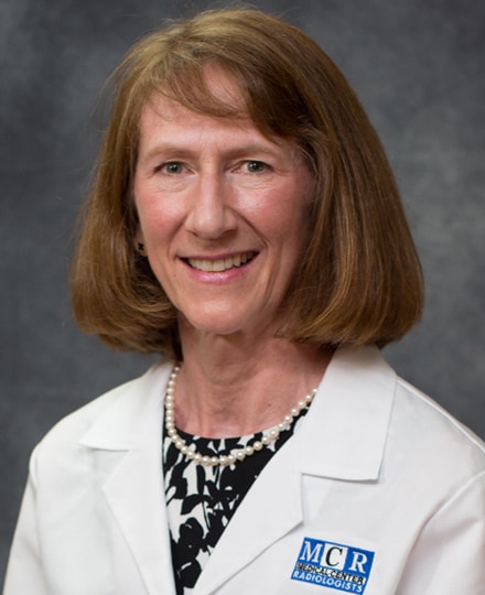 Sarah shaves, md smiling in front of a gray backdrop.