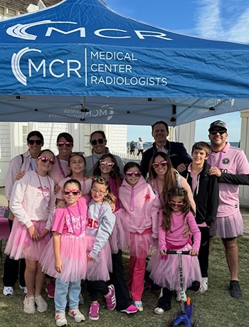 Group photo of adults and children wearing pink outfits standing together under a blue medical center radiologists tent at the making strides against breast cancer walk.