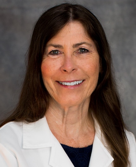 Dr. Susan mckenzie smiling in front of a grey backdrop in a professional headshot.